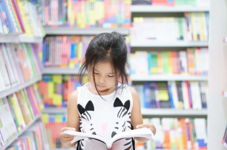 A child reads, surrounded by shelves of books.